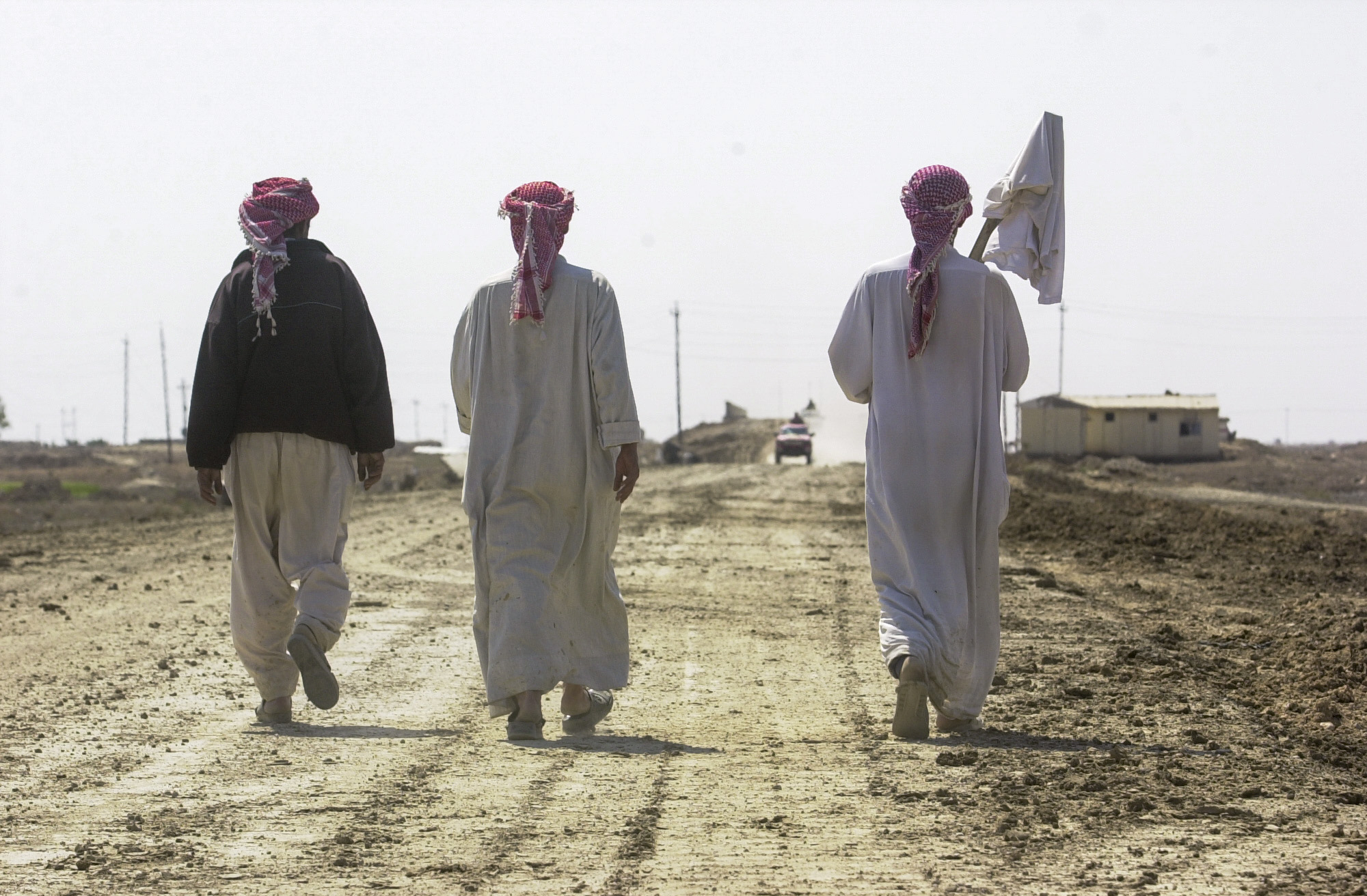 Villagers from the village of As Samawah walk past U.S. Army 7th Cavalry positions outside the city, as smoke billows in the background from a weapons depot struck in the city. The Cavalry has been fighting in and around the town for more than 48 hours, facing at times strong resistence from the fighters inside. (Warren Zinn/Army Times)