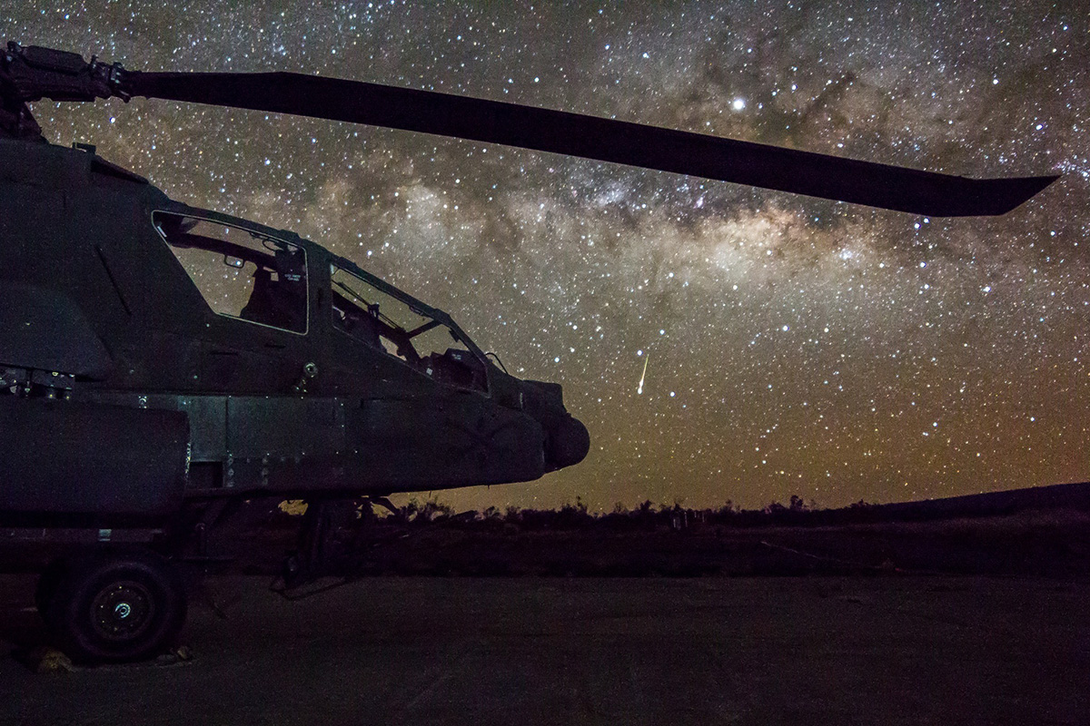 Army AH-64 Apache attack helicopter sits on the flight line April 13, 2019, while a shooting star falls in the sky on FARP 17, Pōhakuloa Training Area, Hawaii. (Capt. Keith Kraker/Army)