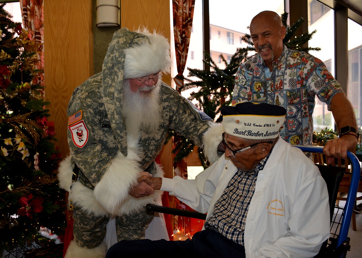 Ray Chavez, the oldest Pearl Harbor survivor, greets William Davis, “the American Santa,” on Dec. 8, 2017, at the Tripler Army Medical Center dining facility in Honolulu, Hawaii, with Joel Jenkins, Tripler protocol officer. (Leanne Thomas/Tripler Army Medical Center)