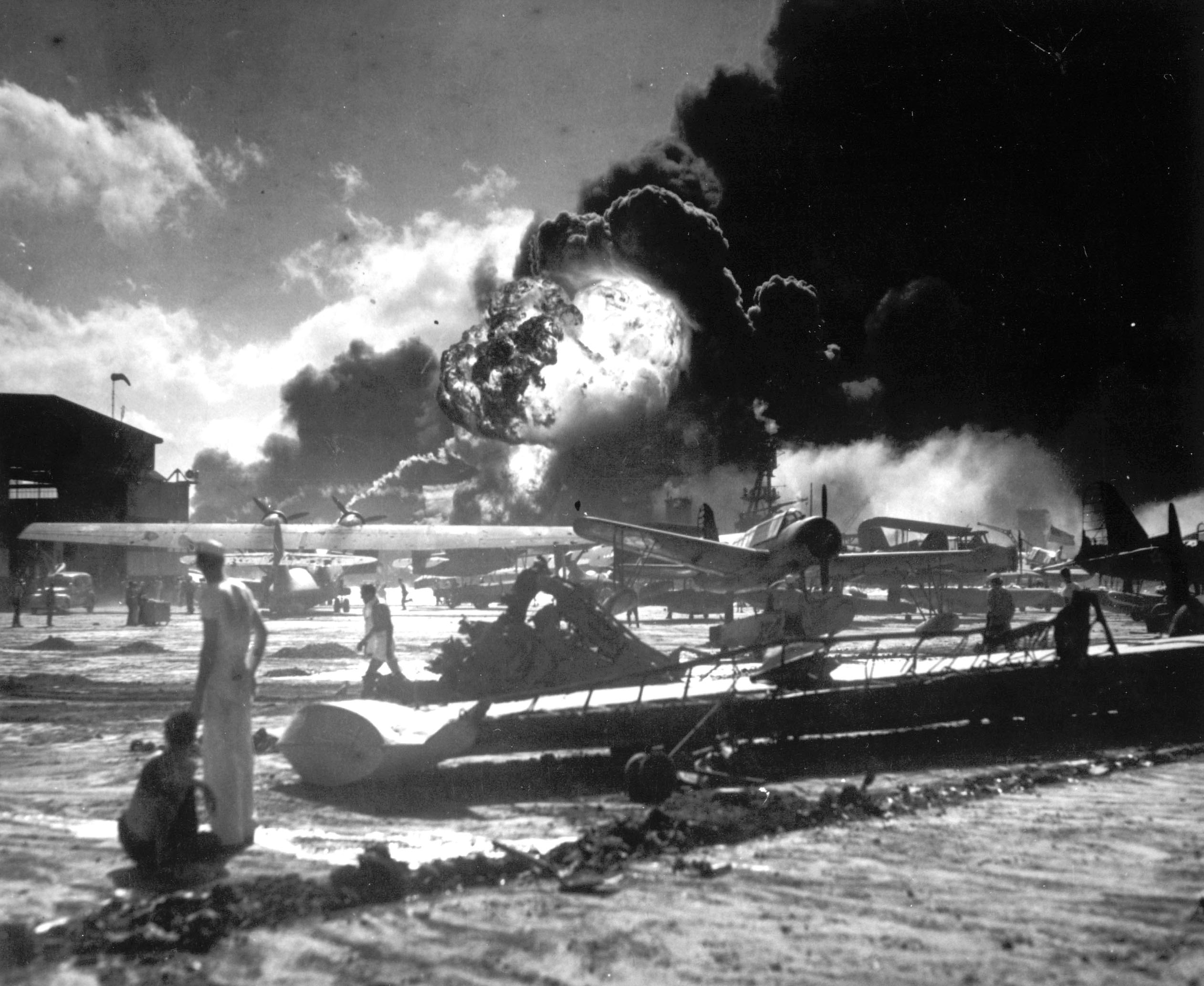 In this image provided by the U.S. Navy, sailors stand among wrecked airplanes at Ford Island Naval Air Station as they watch the explosion of the USS Shaw in the background, during the Japanese surprise attack on Pearl Harbor, Hawaii, on December 7, 1941. (AP Photo/U.S. Navy)