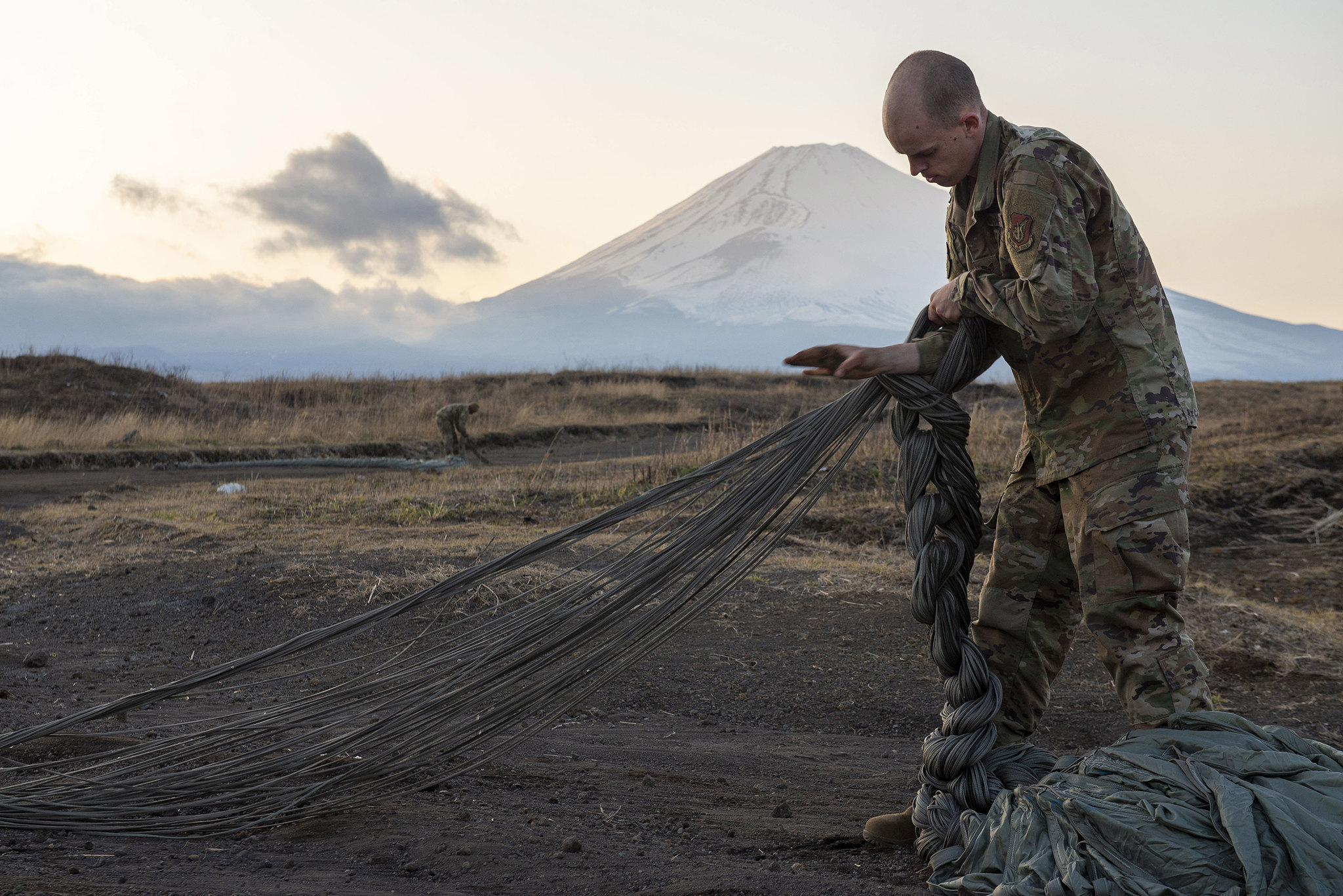 Staff Sgt. Nicholas Adkins folds parachute suspension lines on March 25, 2020, before stowing the parachute inside a recovery bag at the Combined Arms Training Center, Camp Fuji, Japan. (Senior Airman Gabrielle Spalding/Air Force)