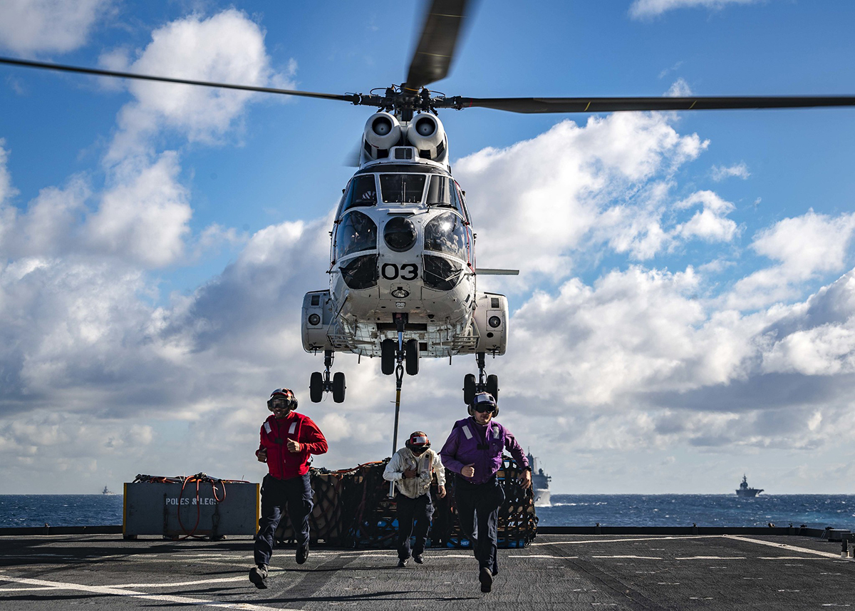 Sailors run past the foul line as a SA-330J Puma picks up pallets from the flight deck of the amphibious dock landing ship USS Ashland (LSD 48) on June 25, 2019, prior to a replenishment-at-sea with the amphibious assault ship USS Wasp (LHD 1) and fleet replenishment oiler USNS Rappahannock (T-AO 204). (Mass Communication Specialist 2nd Class Markus Castaneda/Navy)