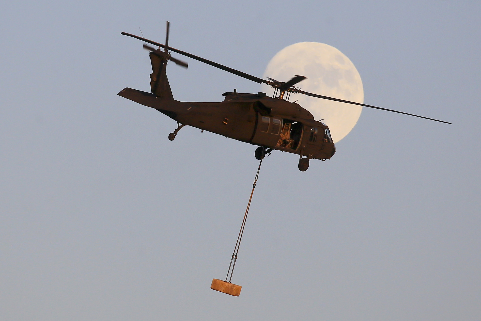 A New Jersey National Guard UH-60 Black Hawk from the 1-150 Assault Helicopter Battalion flies with a concrete block in front of the waxing gibbous moon during sling load training at Joint Base McGuire-Dix-Lakehurst, N.J., Dec. 1, 2017. (Master Sgt. Matt Hecht/Air National Guard)