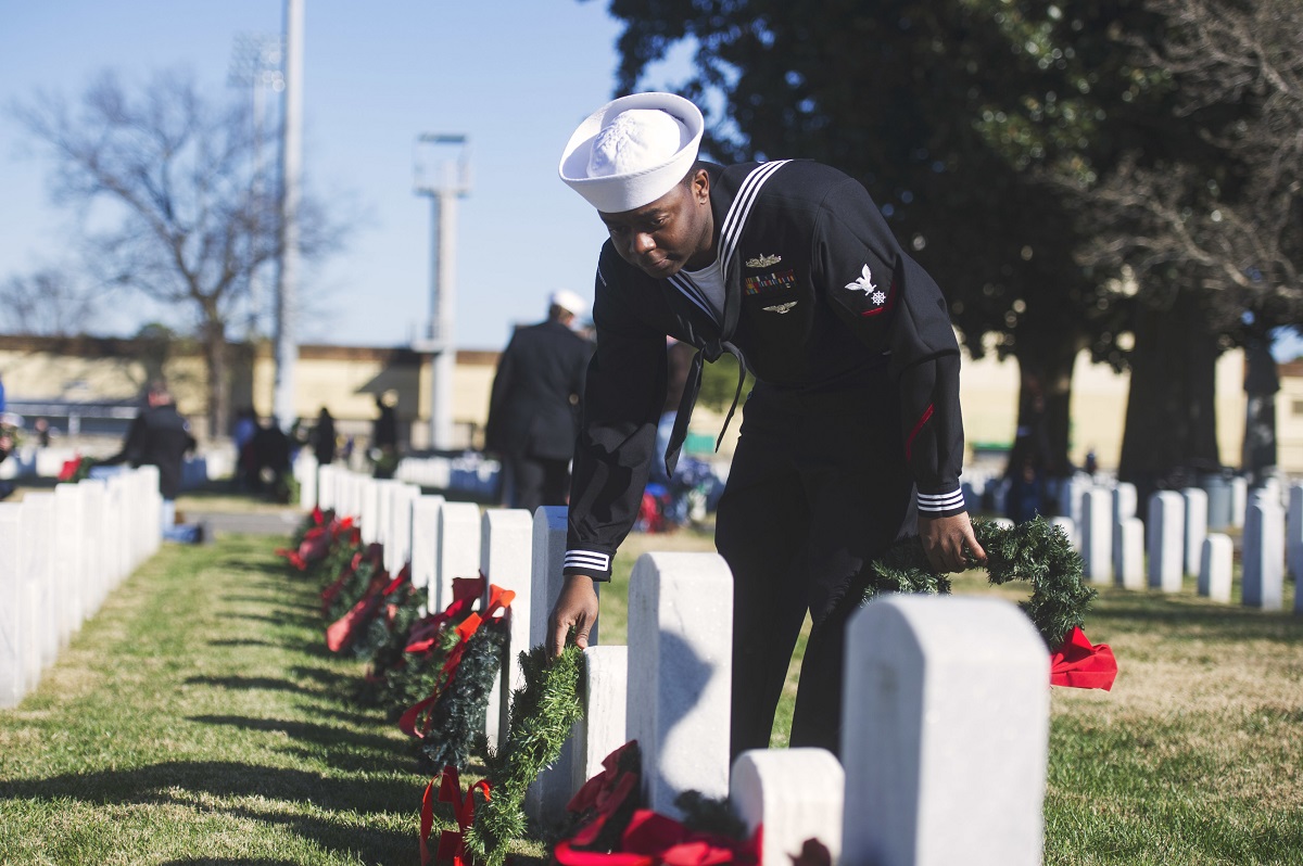 Quartermaster 3rd Class Moise Monestime, assigned to the Nimitz-Class aircraft carrier USS George Washington (CVN 73), lays a wreath on a grave during a Wreaths Across America ceremony Dec. 16, 2017, at Hampton National Cemetery in Virginia. (MC2 Jessica Gomez/Navy)