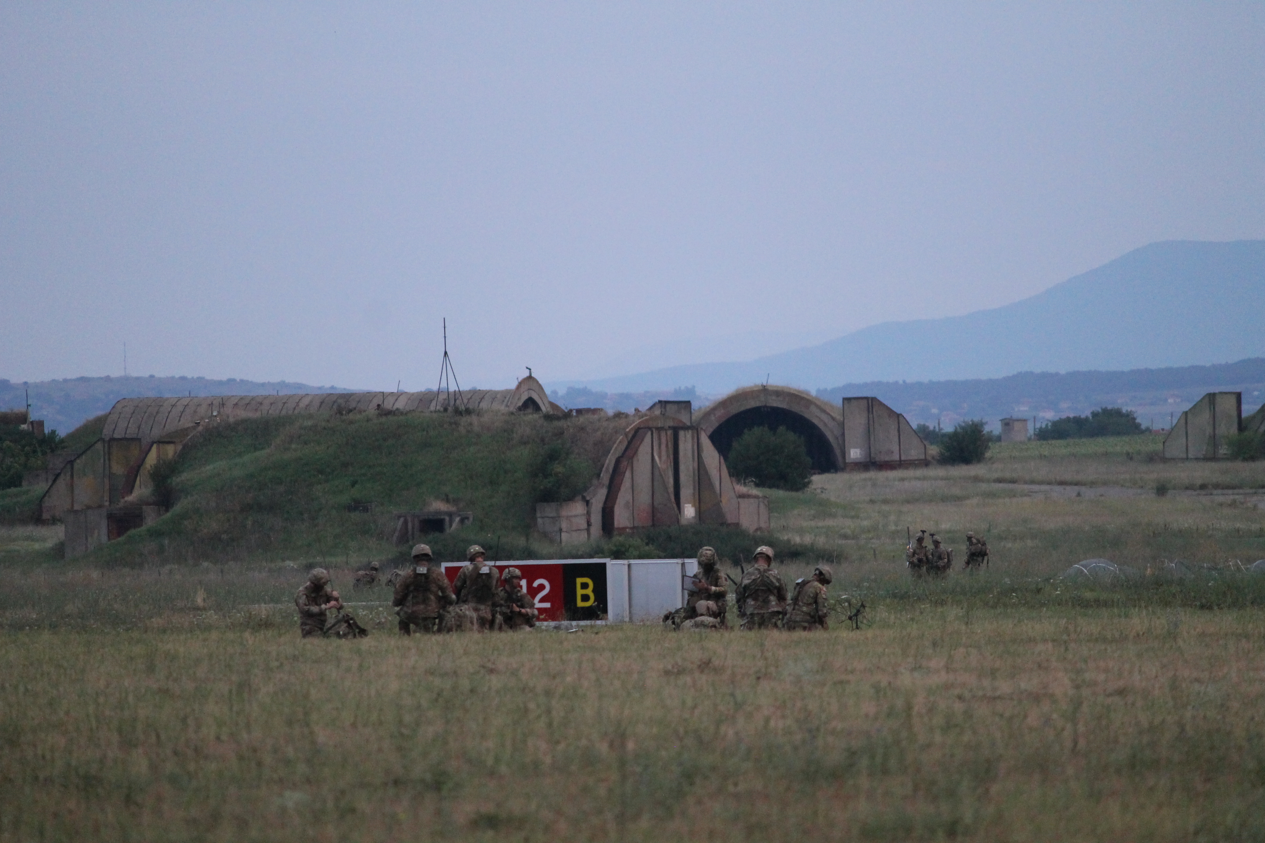 Paratroopers collect on the ground at the perimeter of a series of airplane hangars that collectively look like a hobbit shire. The opposition forces, played by Bulgarian soldiers, sporadically fired at the paratroopers. In a real operation, paratroopers would not land directly in front of the enemy, but for the purposes of observing, everything is designed to happen in close proximity. (Jen Judson/Staff)