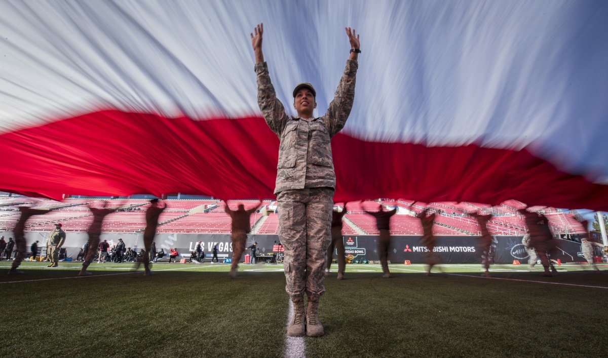 Airman 1st Class Ashley Libby, a 99th Medical Operations Squadron aerospace medical technician at Nellis Air Force Base, Nev., raises her arms to keep the American flag off the ground during the 2018 Las Vegas Bowl opening ceremony at Sam Boyd Stadium in Las Vegas, Dec. 15, 2018. The half-ton flag required more than 200 airmen to carry it. (Senior Airman Andrew D. Sarver/Air Force)
