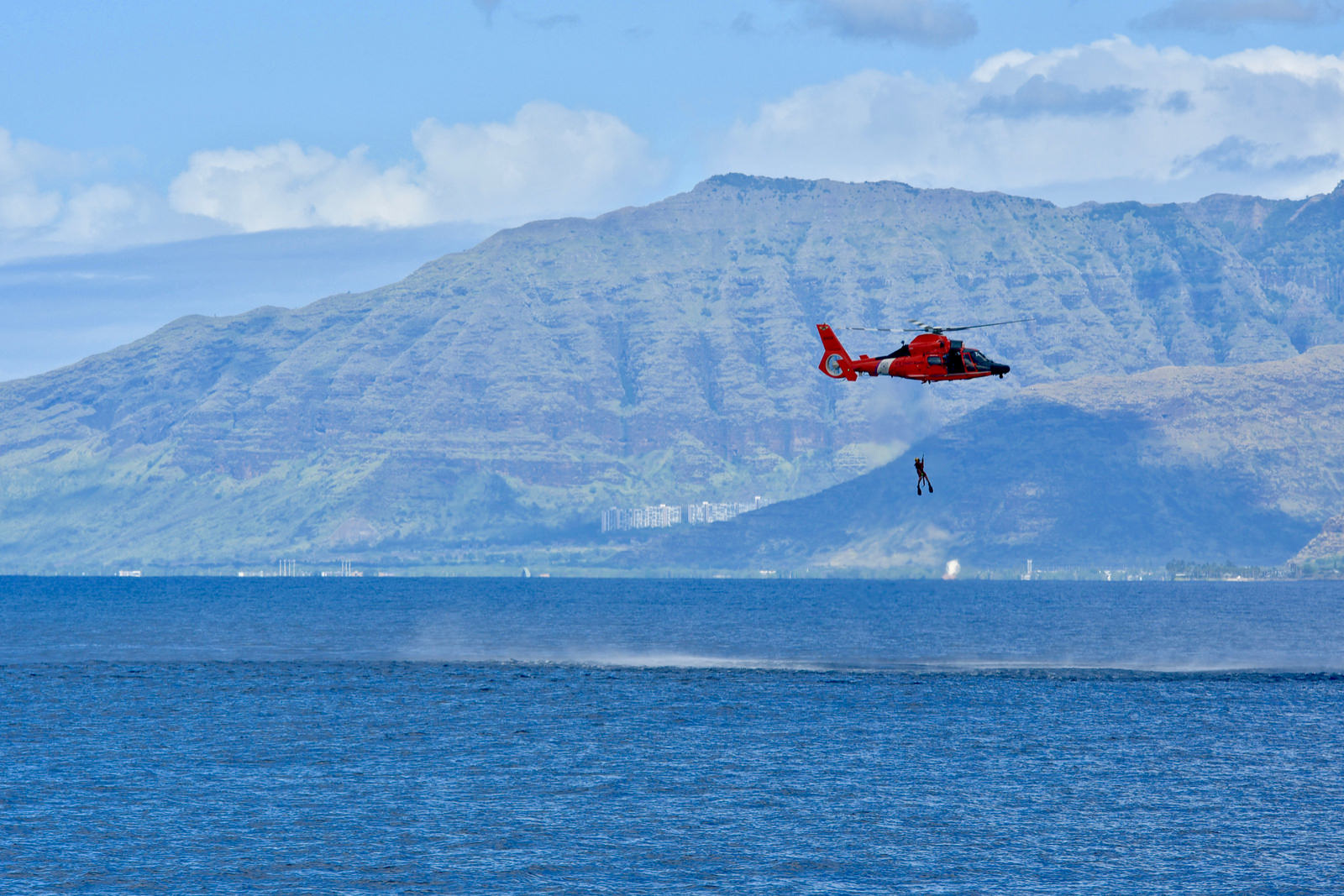 The crew of an Air Station Barbers Point MH-65 Dolphin helicopter raises their rescue swimmer during a search-and-rescue exercise in the vicinity offshore from Ko'olina to Kahe Point, Oahu, on Nov. 29, 2018. (Lt. j.g. Joshua Martin/Coast Guard)