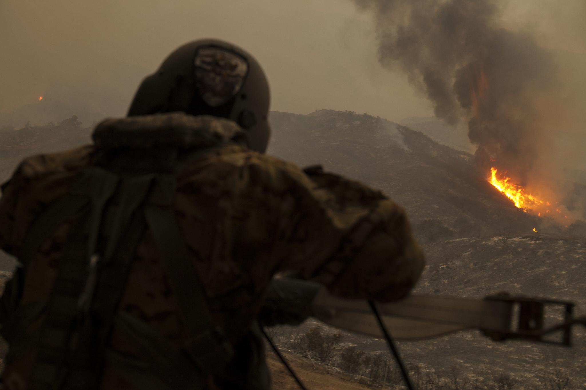 Flames from the Thomas Fire in Ventura County, California, are seen as Sgt. Anthony Orduno, a UH-60 Black Hawk helicopter crew chief from the California Army National Guard's B Company, 1st Battalion, 140th Aviation Regiment, looks on while flying overhead. Orduno and the helicopter crew spent the day dropping water on the fire in coordination with CAL FIRE. (U.S. Air National Guard photo by Senior Airman Crystal Housman)
