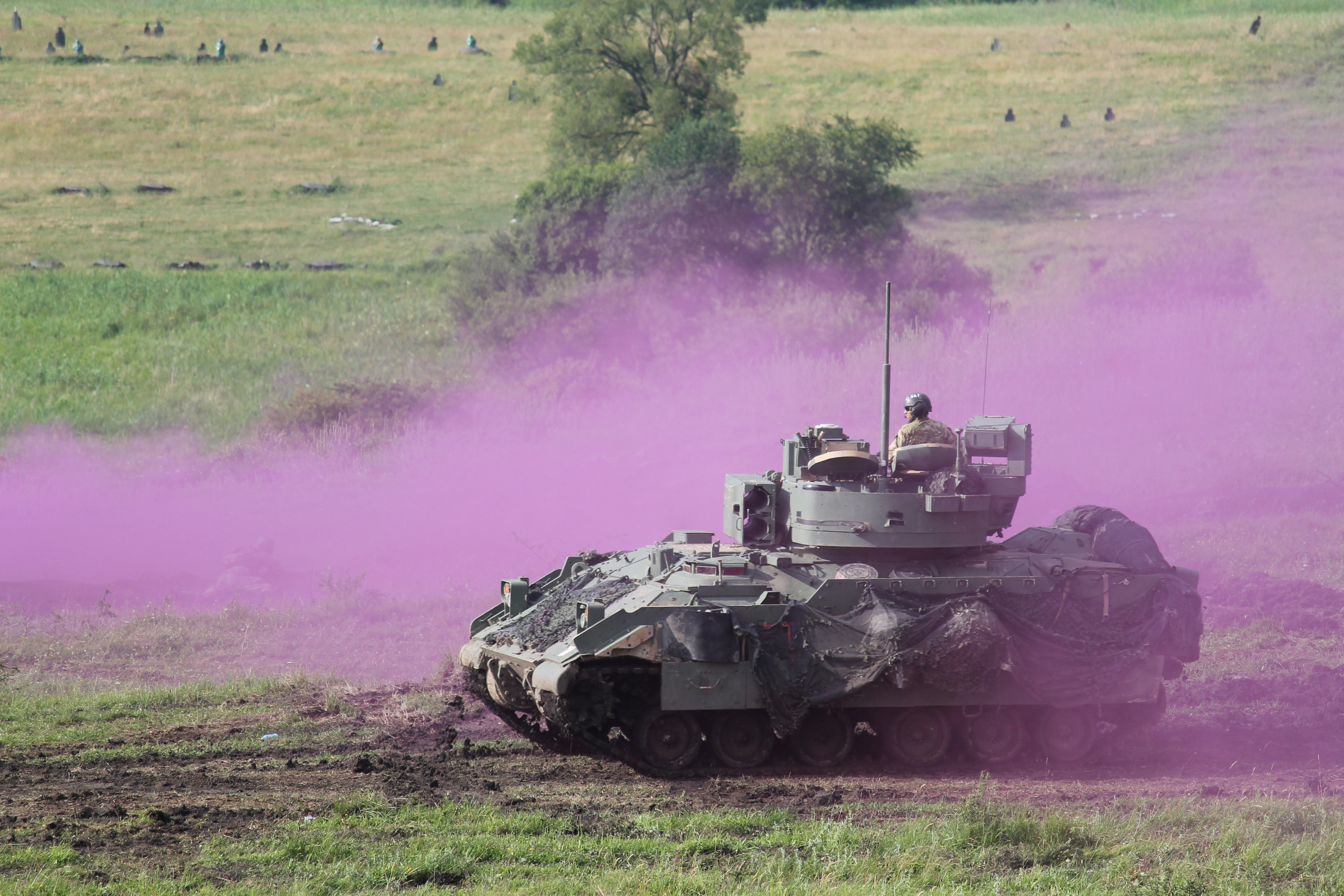 A Bradley Fighting Vehicle moves into fighting position amid the purple haze of a smoke obscurant meant to conceal friendly infantry moving toward battle positions. (Jen Judson/Staff)