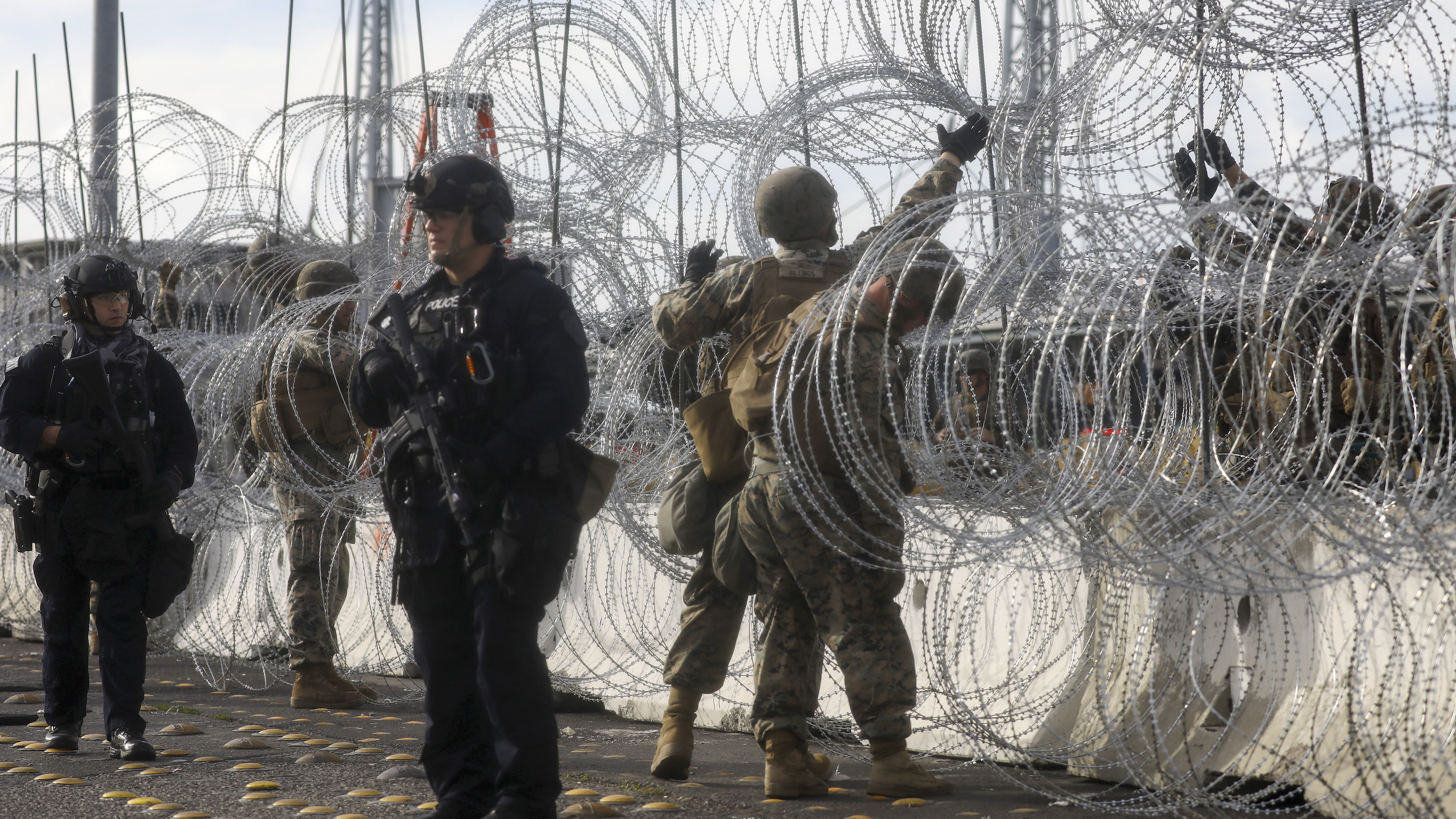 U.S. Customs and Border Protection (CBP) agents (L) stand watch as U.S. Marines handle concertina wire at the San Ysidro port of entry during a