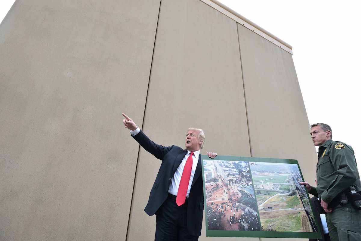 U.S. President Donald Trump holds up a poster of before and after photos of a segment of the border wall prototypes with Chief Patrol Agent Rodney S. Scott, right, in San Diego, Calif., on March 13, 2018. (Mandel Ngan/AFP via Getty Images)