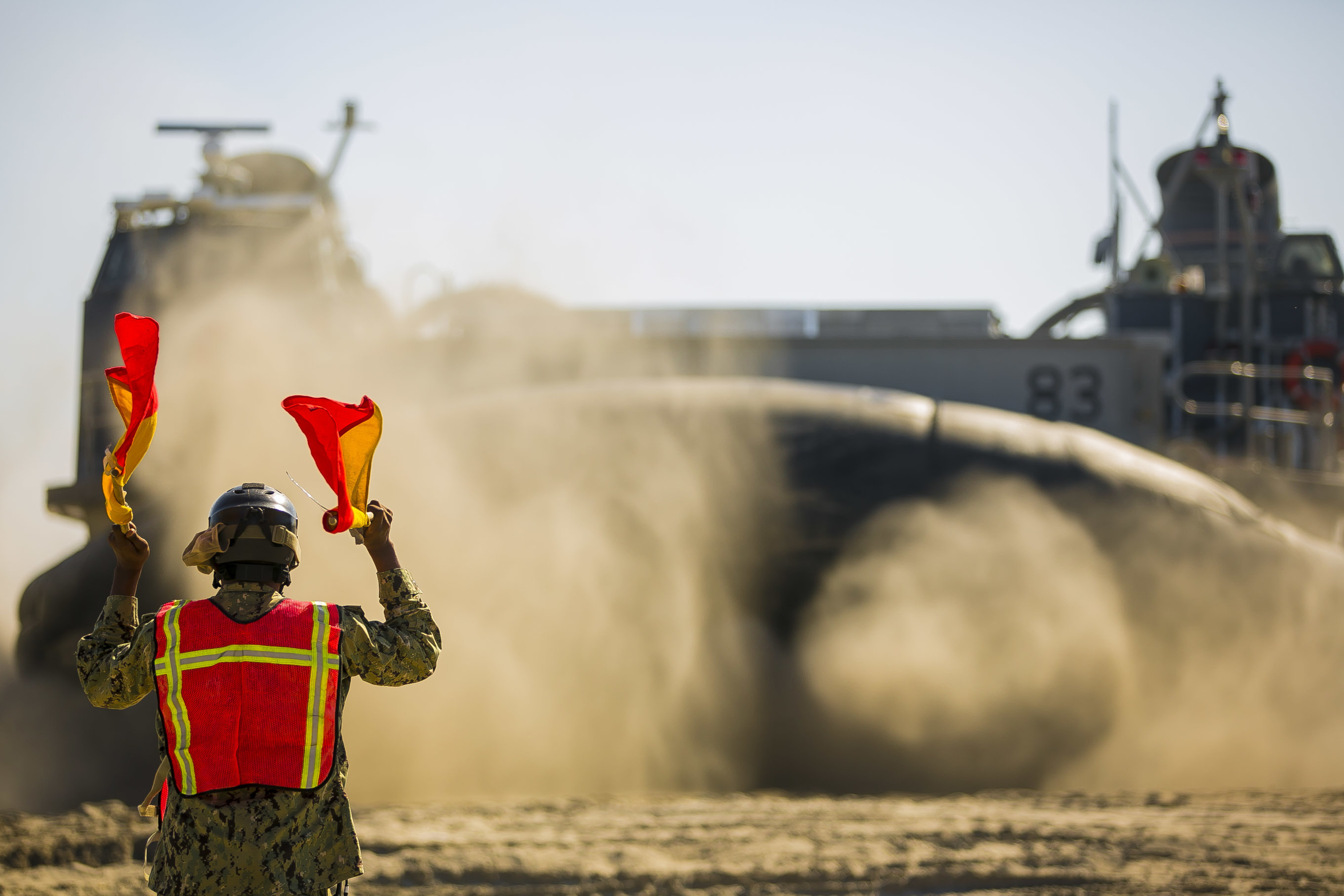 A U.S. Navy sailor signals Landing Craft, Air Cushion 83, to embark on the amphibious assault ship USS Iwo Jima (LHD-7) as part of a Composite Training Unit Exercise (COMPTUEX) at Onslow Beach. (Staff Sgt. Dengrier M. Baez/Marine Corps)