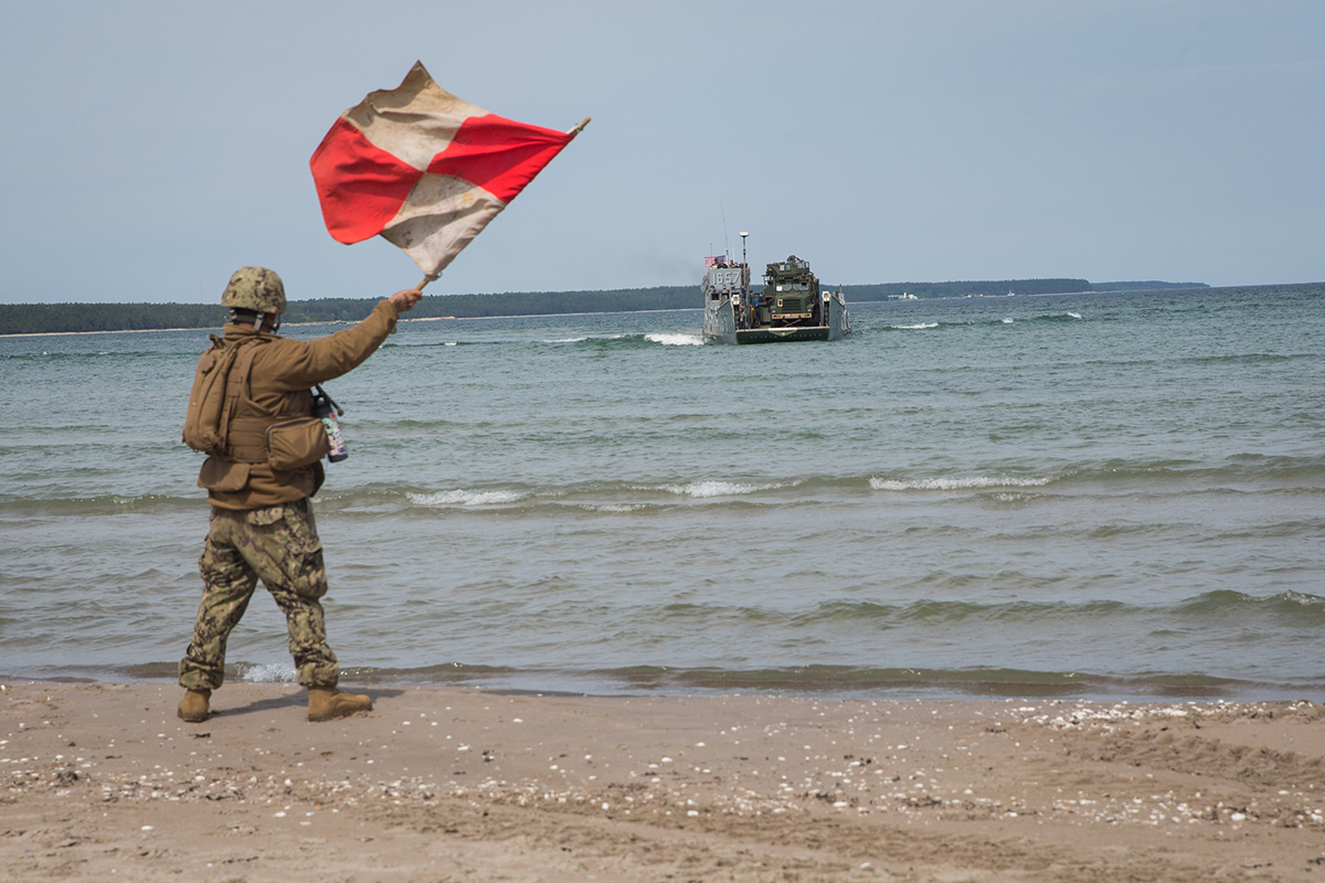 A sailor signals a U.S. Navy landing craft, utility on June 12, 2019, to offload tactical vehicles during Exercise Baltic Operations 2019 in Kallaste, Estonia. (Cpl. Abrey Liggins/Marine Corps)